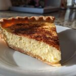 A perfect slice of creamy custard pie dusted with cinnamon on a white plate.