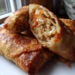 Close-up of a crispy, golden brown egg roll cut open to show the savory filling of meat, cabbage, and carrots.
