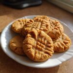 A stack of golden brown peanut butter cookies with classic crisscross fork marks, served on a white plate.