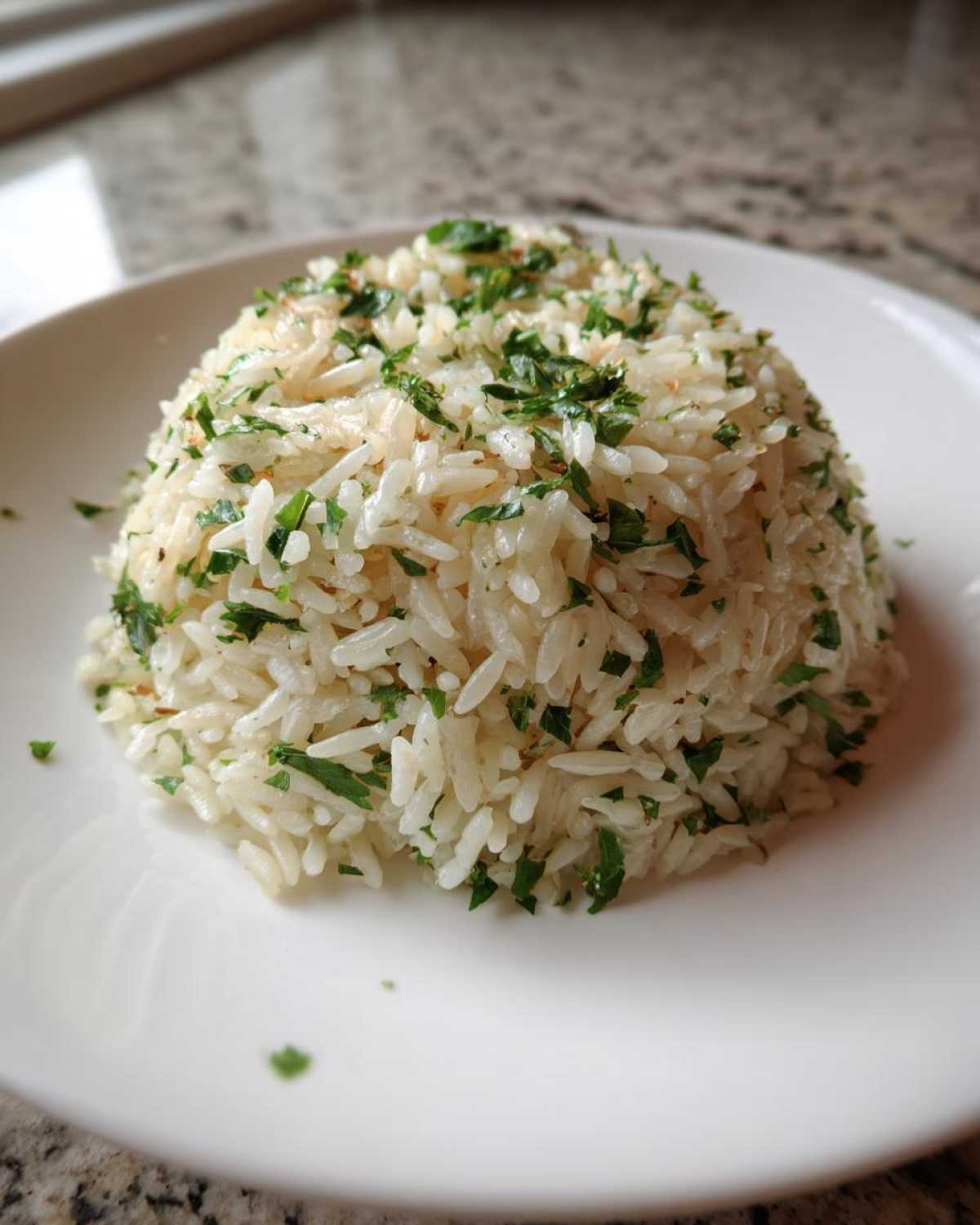 A mound of fluffy white rice pilaf topped generously with chopped fresh green parsley on a white plate.