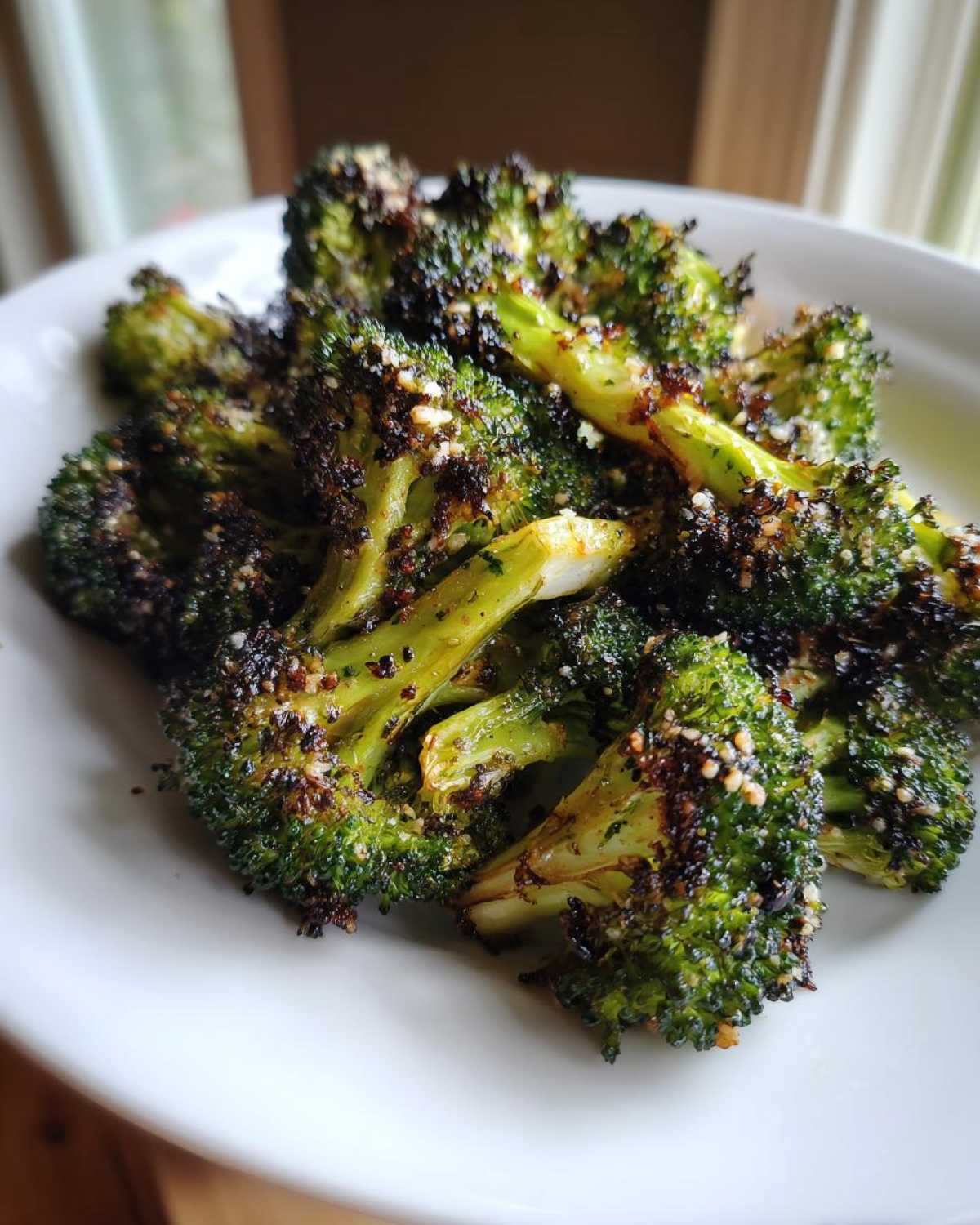 Close-up of perfectly charred and seasoned roasted broccoli florets served on a white plate.