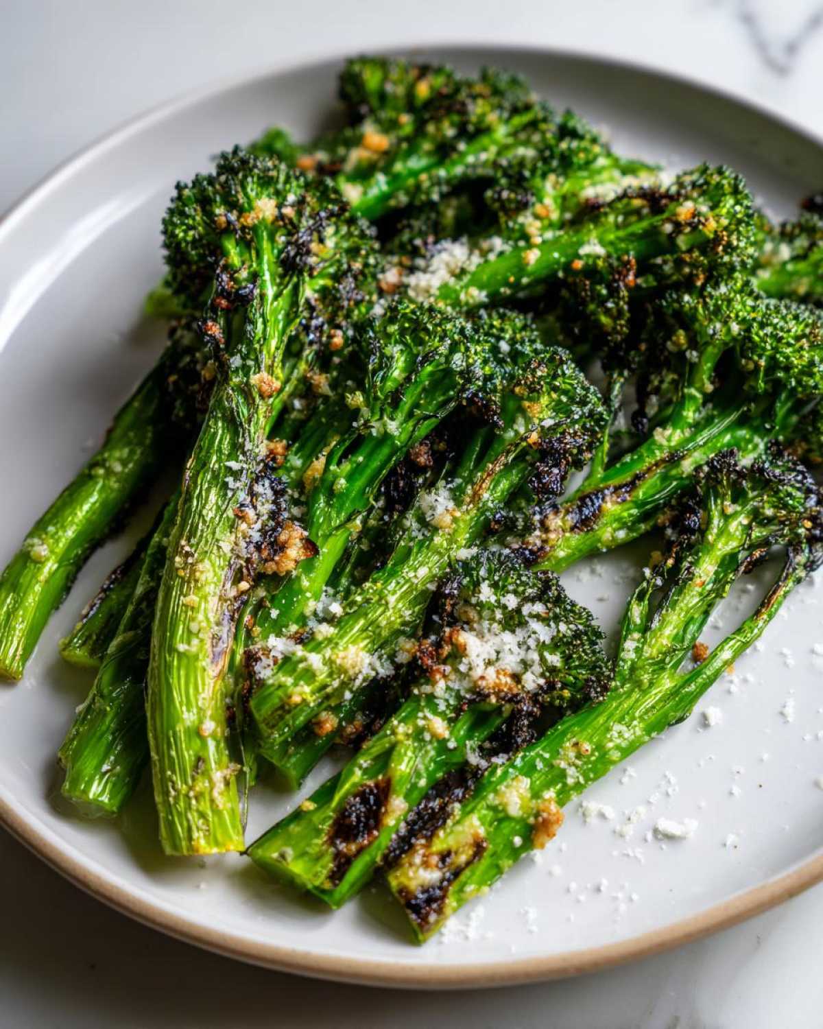 Close-up of bright green roasted broccoli stalks topped with grated Parmesan cheese and crispy bits.