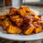 A pile of perfectly caramelized roasted sweet potato cubes piled high on a white plate.