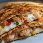 Close-up of a perfectly grilled shrimp quesadilla slice showing melted white cheese, seasoned shrimp, and colorful bell peppers.