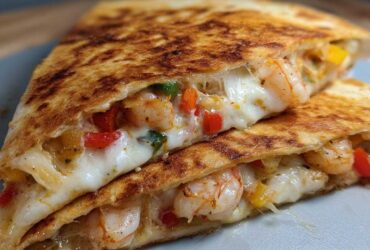 Close-up of a perfectly grilled shrimp quesadilla slice showing melted white cheese, seasoned shrimp, and colorful bell peppers.
