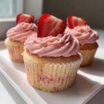 Three delicious strawberry cupcakes topped with pink frosting and fresh strawberry slices, ready to eat.
