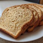 Four golden-brown slices of homemade whole wheat bread fanned out on a white plate.