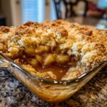 Close-up of a freshly baked apple cobbler recipe with a thick, golden crumble topping and gooey apple filling.