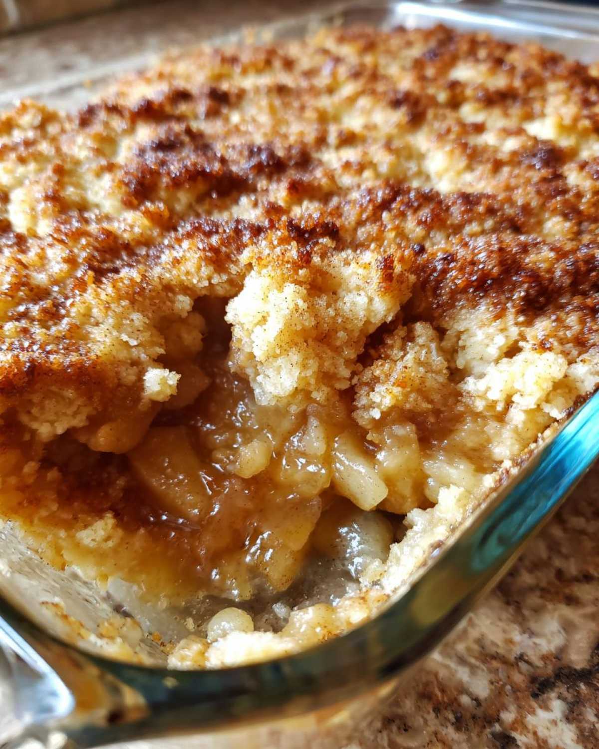 Close-up of a freshly baked apple cobbler recipe, showing the gooey, spiced apple filling beneath a golden, crumbly topping.