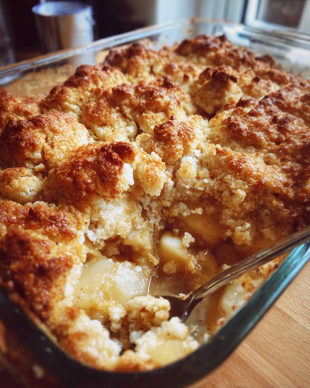 Close-up of a freshly baked apple cobbler recipe with a golden, crumbly topping being scooped with a spoon.