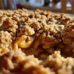 A close-up view showing the gooey, spiced apples beneath a thick, golden-brown, crunchy topping of an apple crisp recipe.