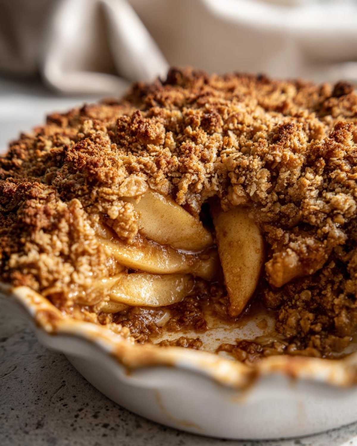 A close-up, cross-section view of a baked apple crisp recipe showing soft, caramelized apple slices beneath a thick, golden-brown oat topping.