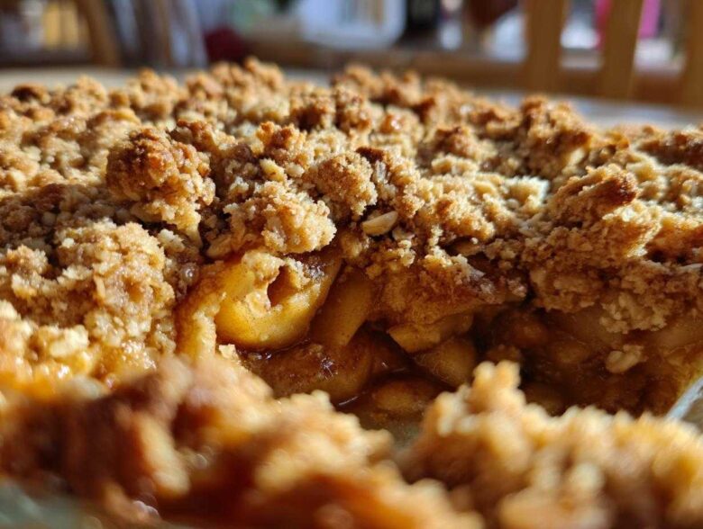 A close-up view showing the gooey, spiced apples beneath a thick, golden-brown, crunchy topping of an apple crisp recipe.