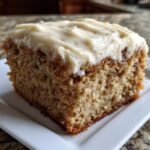 Close-up of a moist slice of applesauce cake topped with thick, creamy frosting.
