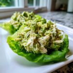 Two servings of creamy avocado chicken salad piled high in bright green lettuce cups on a white plate.