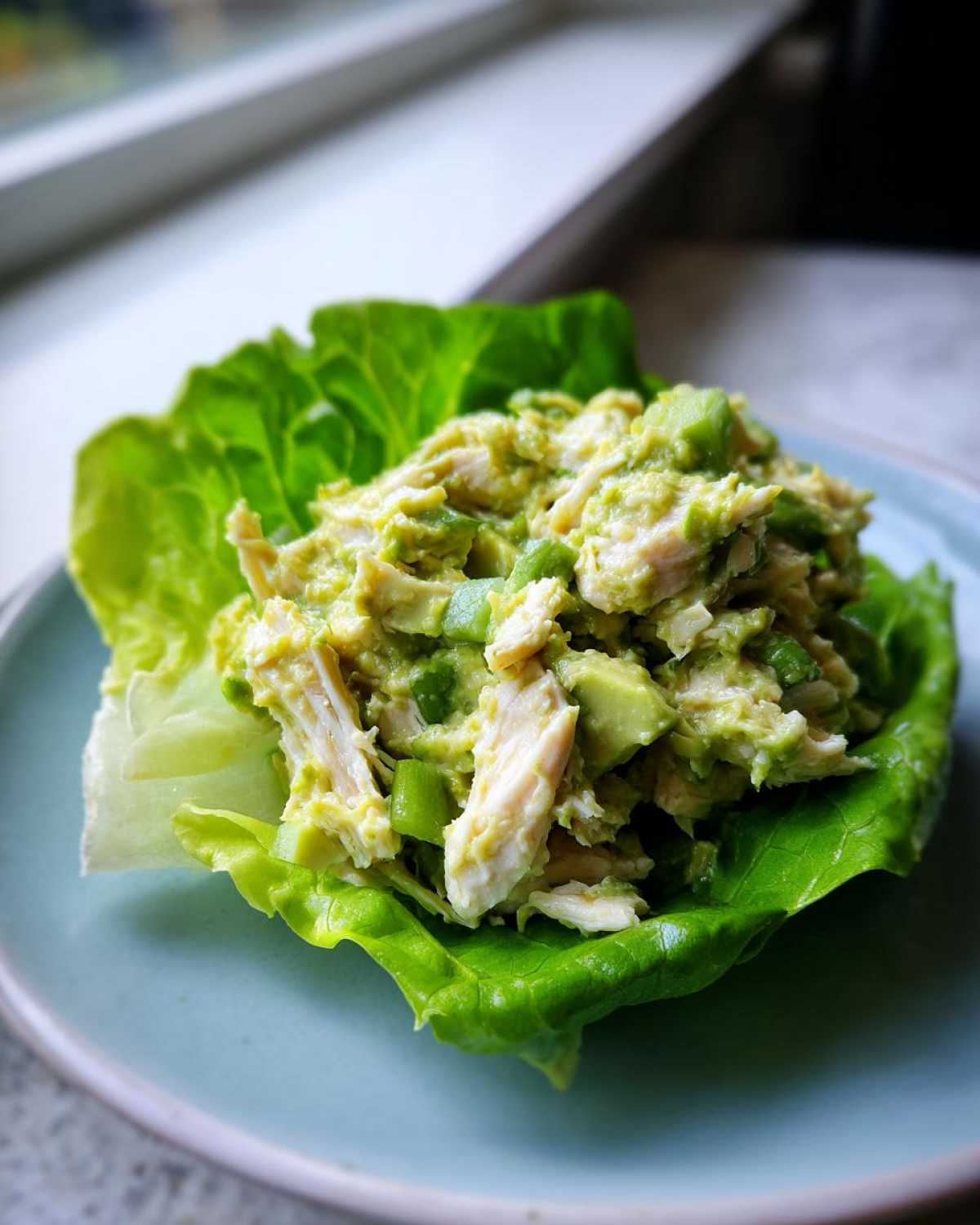 Close-up of creamy avocado chicken salad served in a crisp lettuce cup on a light blue plate.