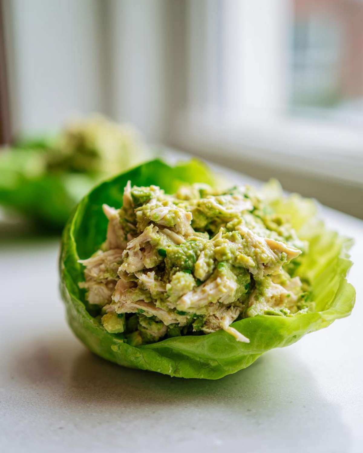 Close-up of creamy avocado chicken salad served inside a crisp butter lettuce cup.