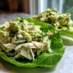 Close-up of creamy avocado chicken salad served in crisp lettuce cups on a white plate.