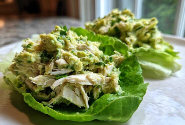 Close-up of creamy avocado chicken salad served in crisp lettuce cups on a white plate.