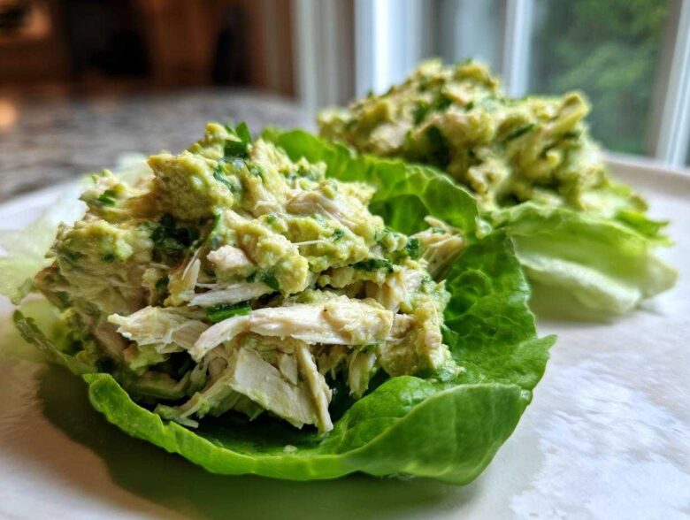 Close-up of creamy avocado chicken salad served in crisp lettuce cups on a white plate.