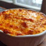 Close-up of a hot, baked Buffalo chicken dip in a white dish with a bubbly, golden-brown cheese topping.