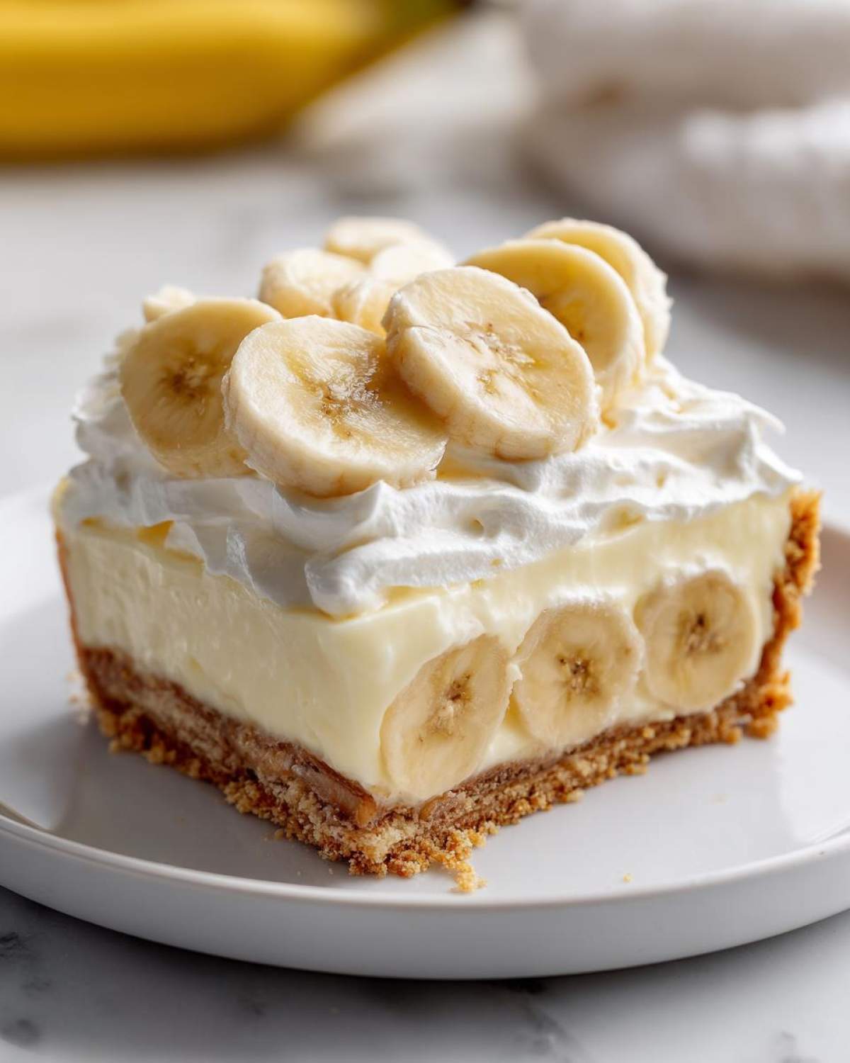 Close-up of a slice of banana cream pie recipe showing graham cracker crust, creamy filling, and fresh banana slices.