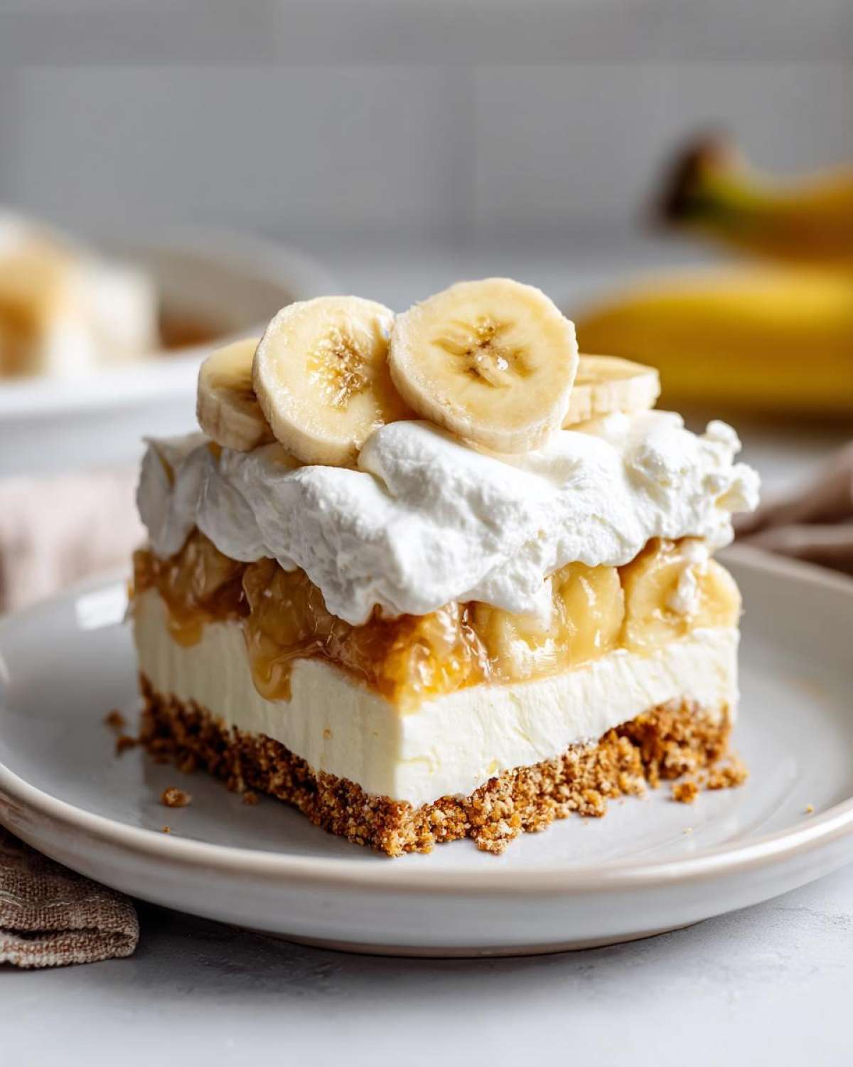 A layered slice of banana cream pie recipe dessert with a graham cracker crust, cream filling, banana topping, and whipped cream.