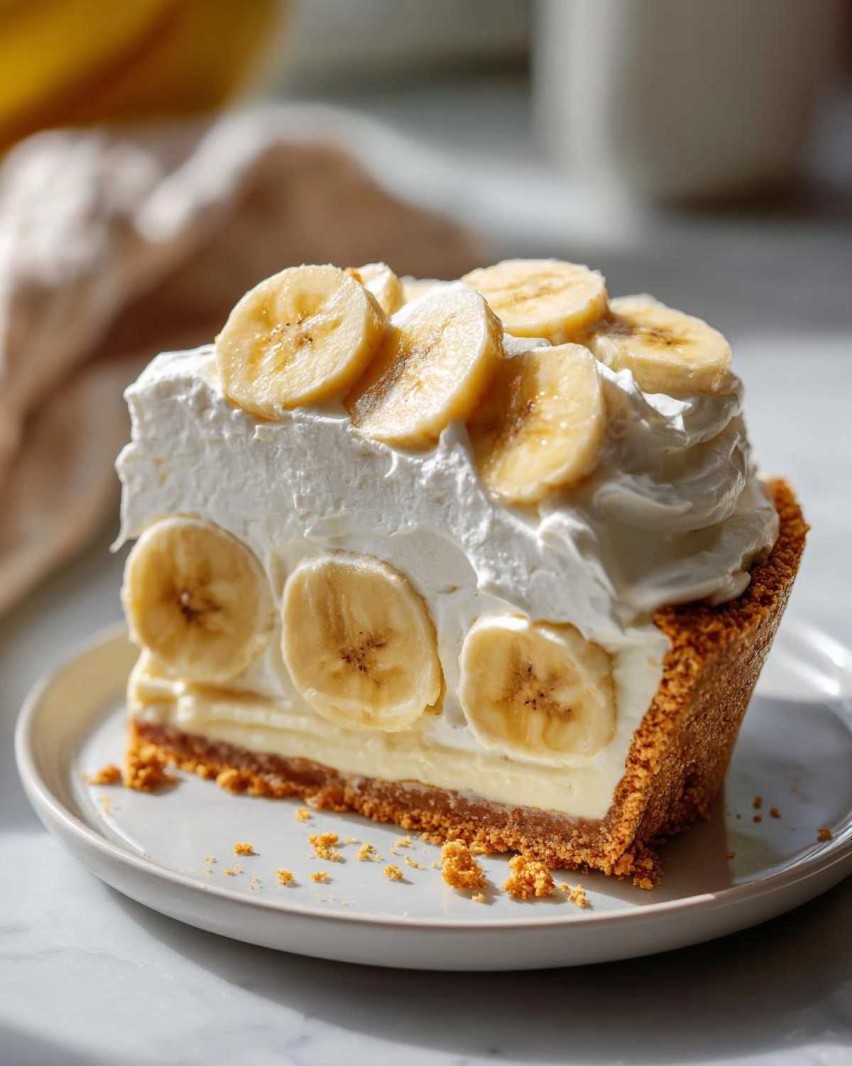 A decadent slice of banana cream pie recipe with a graham cracker crust, creamy filling, and fresh banana slices topped with whipped cream.