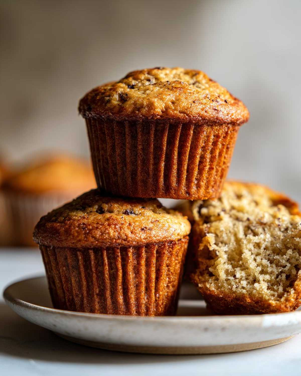 Close-up of two whole banana protein muffins stacked, with one muffin cut in half showing the moist interior.