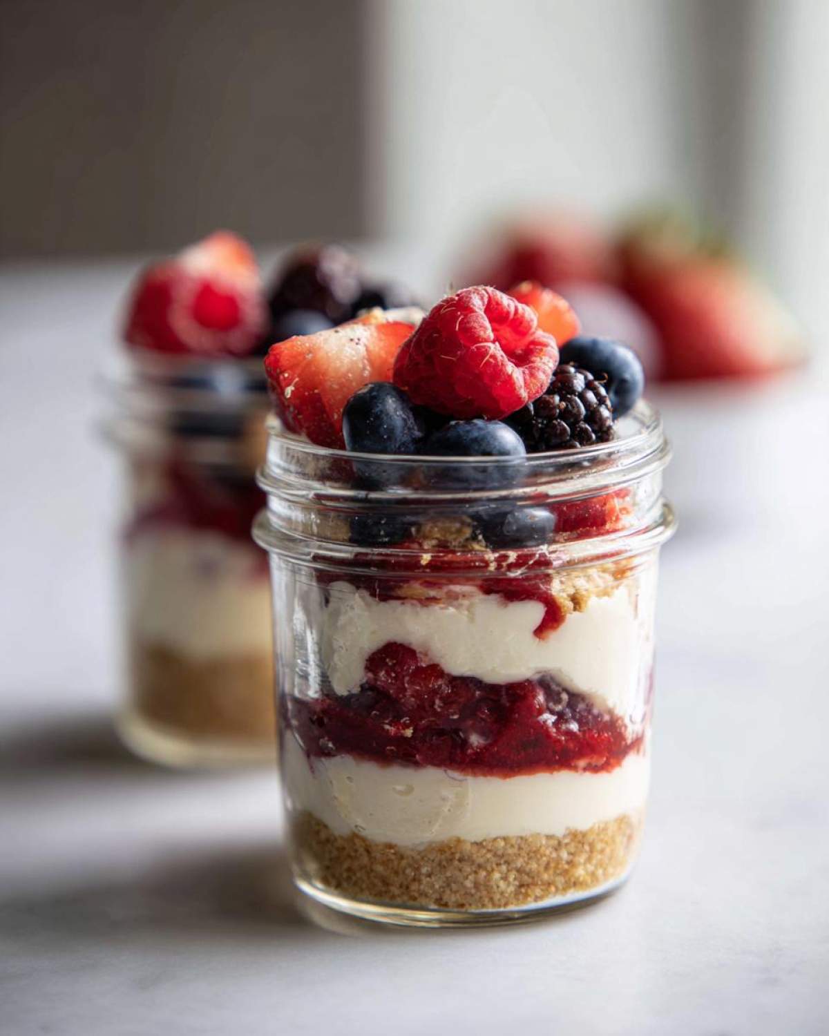 Close-up of a layered Protein Cheesecake in a jar topped with fresh mixed berries.