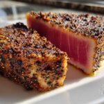 Two thick pieces of perfectly cooked Blackened Tuna Steak, showing a dark spice crust and bright pink, rare center.