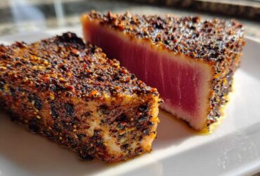 Two thick pieces of perfectly cooked Blackened Tuna Steak, showing a dark spice crust and bright pink, rare center.