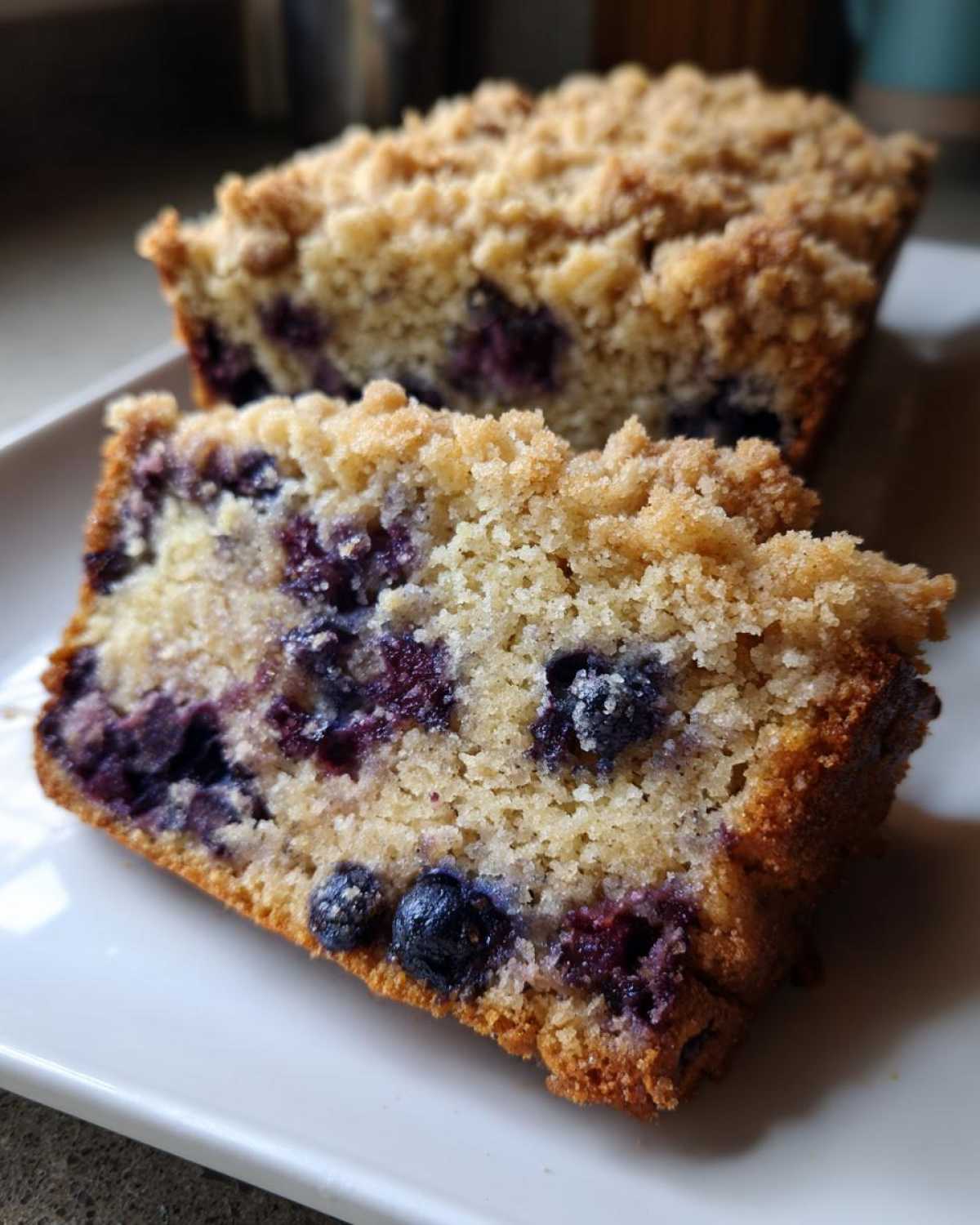 Close-up of a moist slice of blueberry banana bread featuring visible blueberries and a sweet crumb topping.