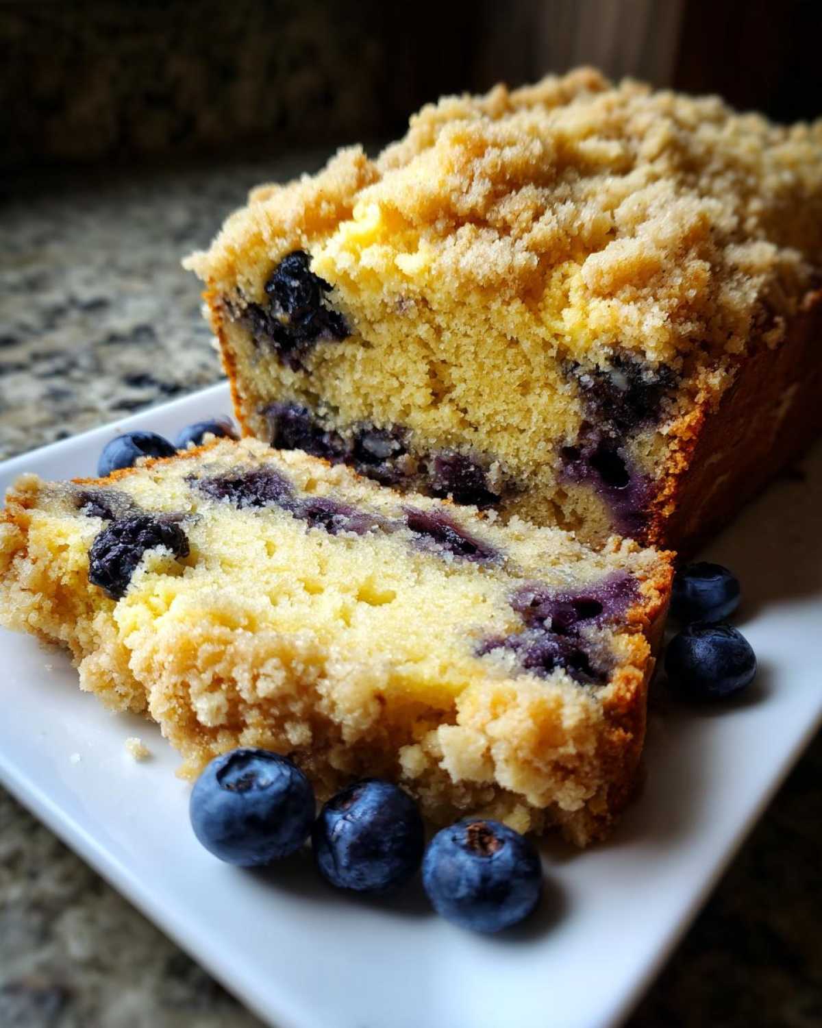A slice of moist blueberry banana bread featuring a thick, golden crumb topping and fresh blueberries.
