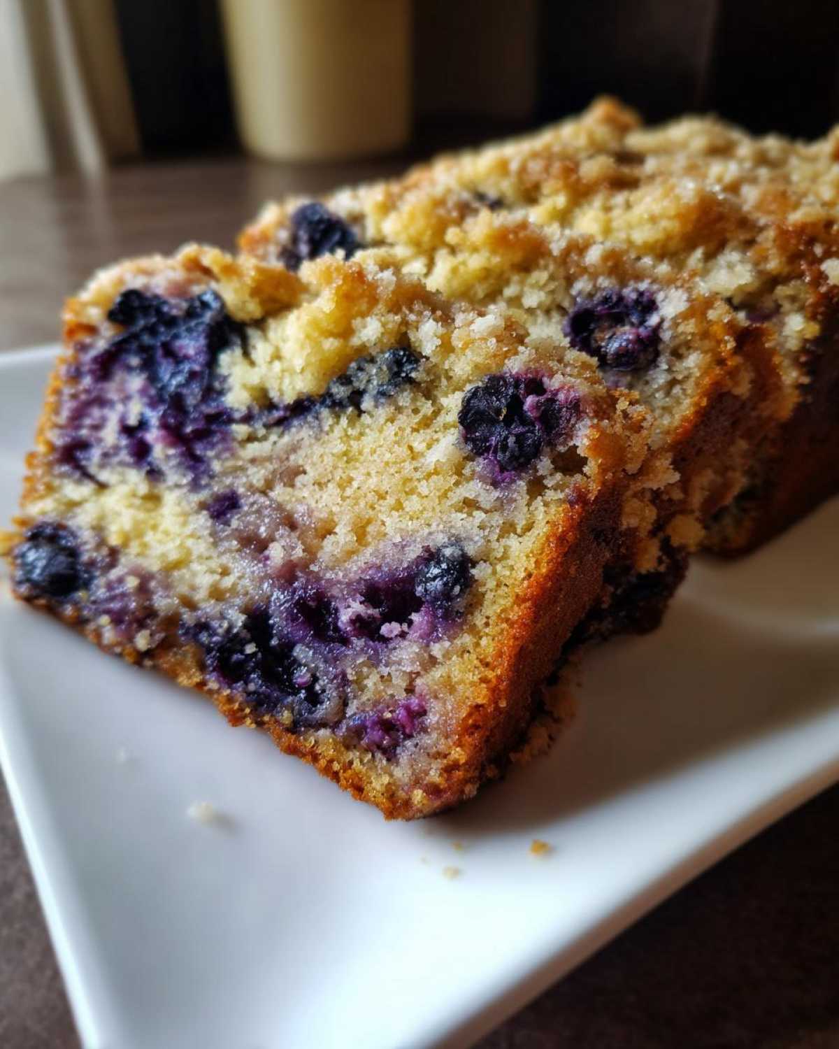 Close-up of moist slices of blueberry banana bread featuring visible blueberries and a sugary crumb topping.
