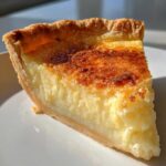 Close-up of a perfect slice of buttermilk pie showing a creamy yellow filling and a deeply caramelized, golden-brown top crust.