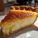 A close-up slice of creamy buttermilk pie showing a golden, caramelized top and flaky crust.