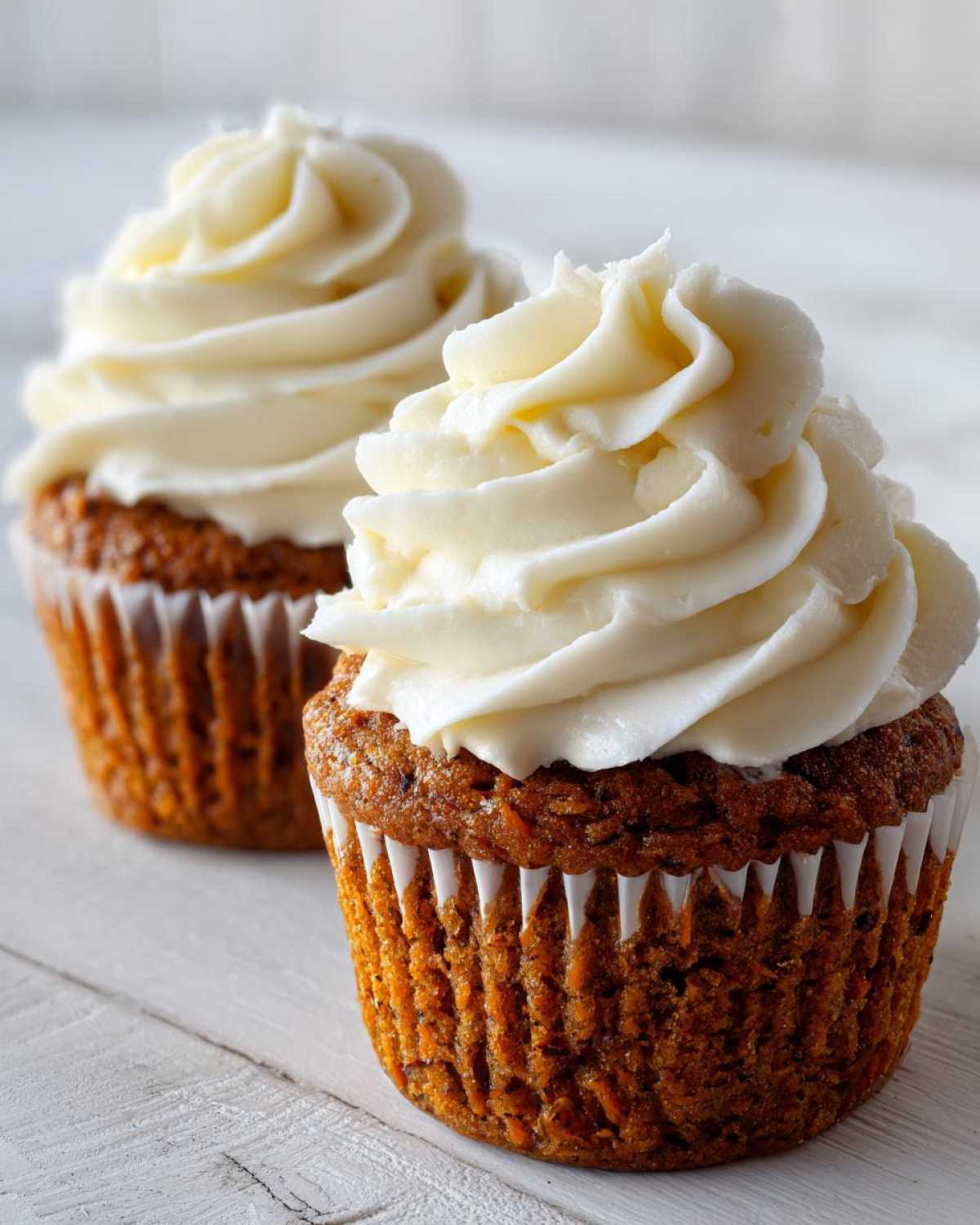 Close-up of two delicious carrot cake muffins topped with thick swirls of cream cheese frosting.