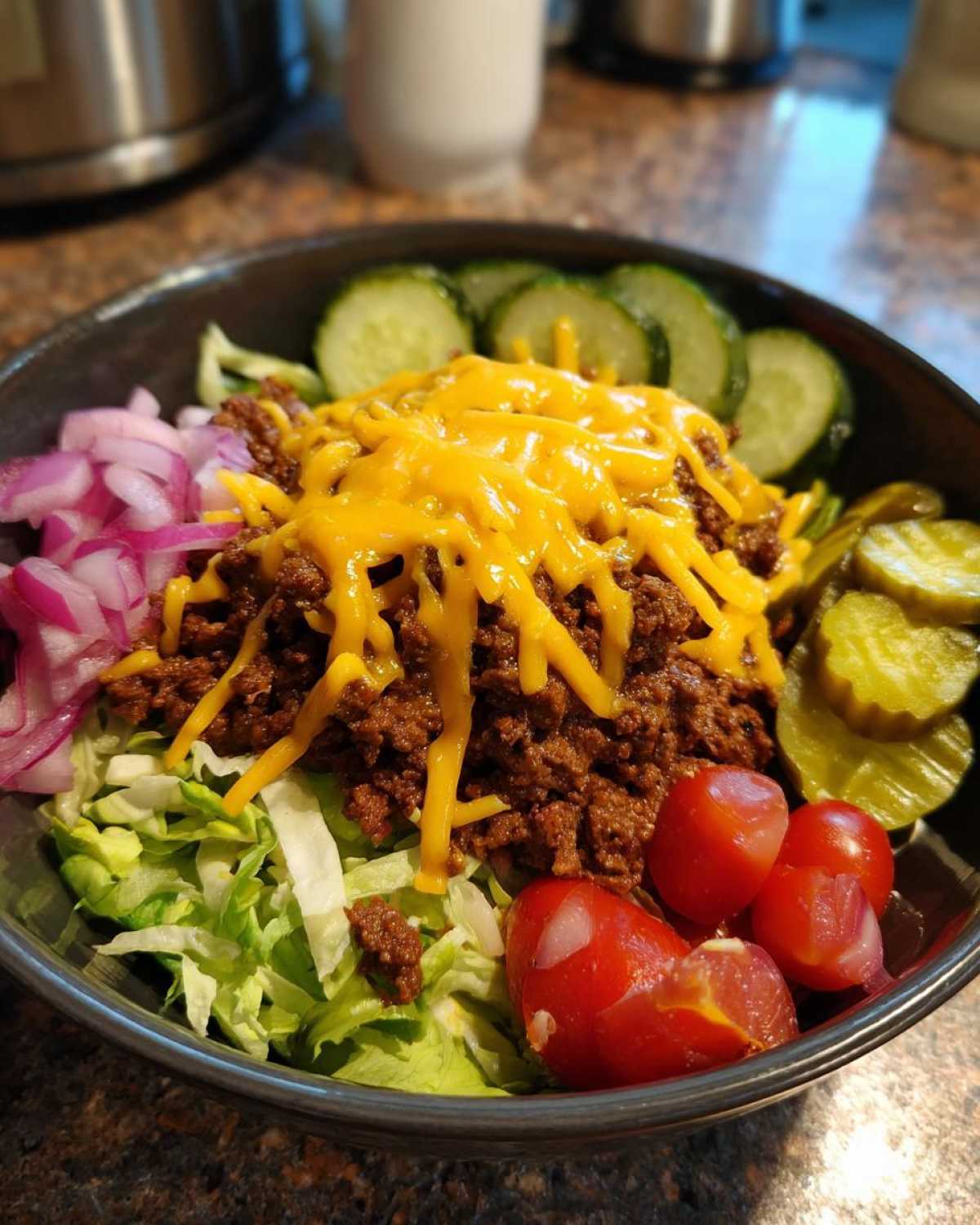 A close-up of a delicious cheeseburger bowl featuring seasoned ground beef, melted cheddar cheese, lettuce, tomatoes, pickles, and red onion.
