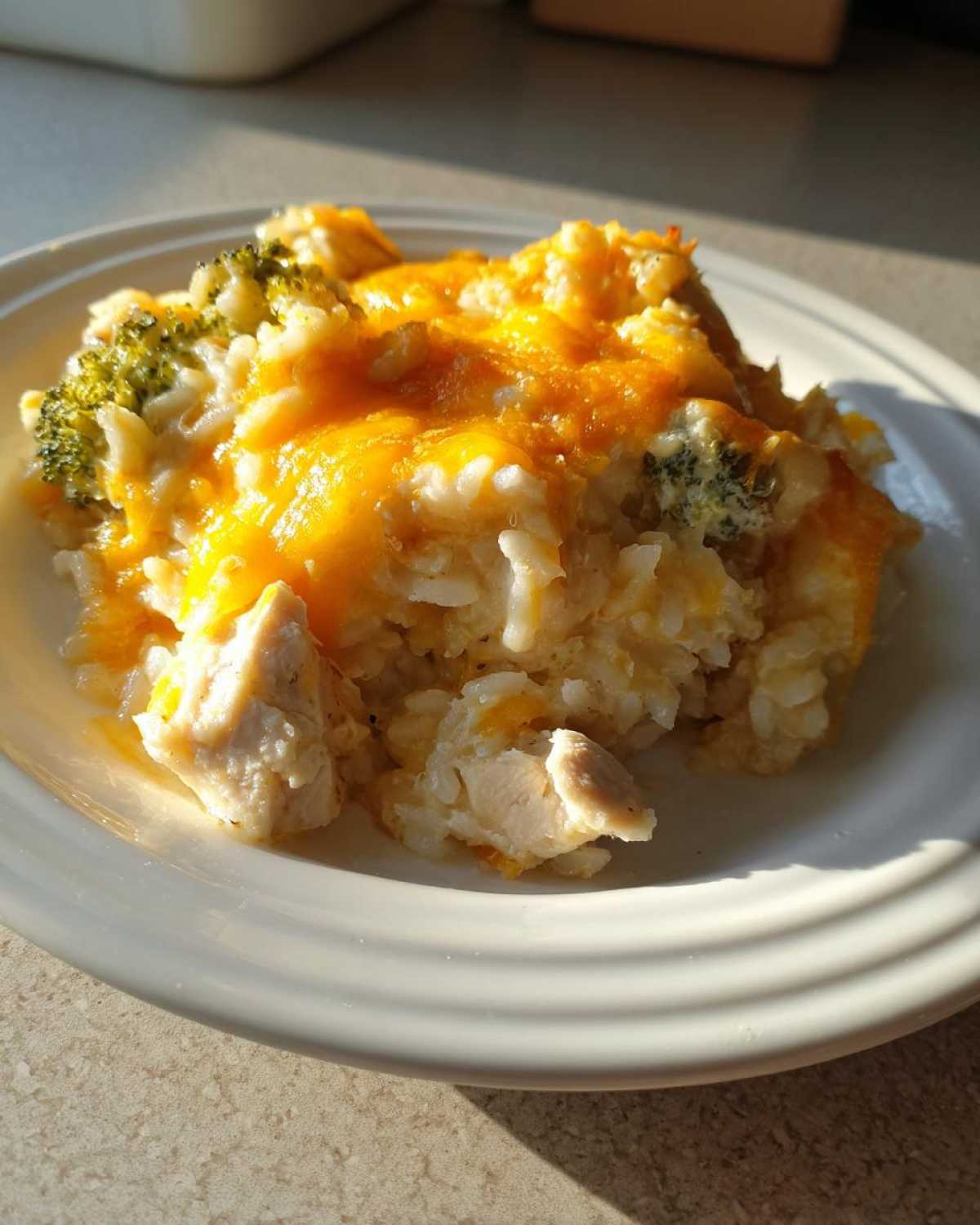 A serving of cheesy chicken and rice casserole topped with melted cheddar cheese and visible broccoli florets.