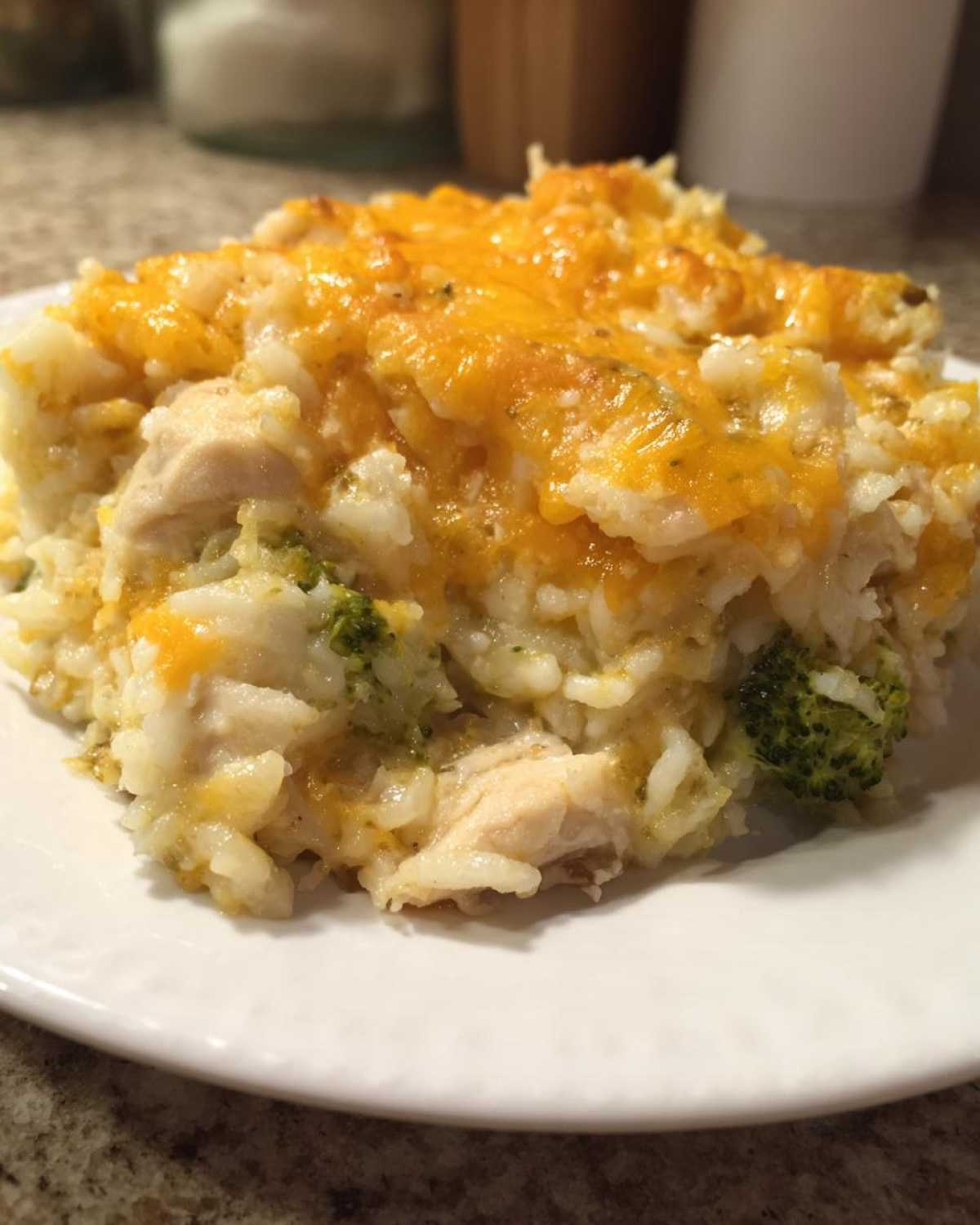 A close-up of a serving of cheesy chicken and rice casserole topped with melted cheddar cheese.