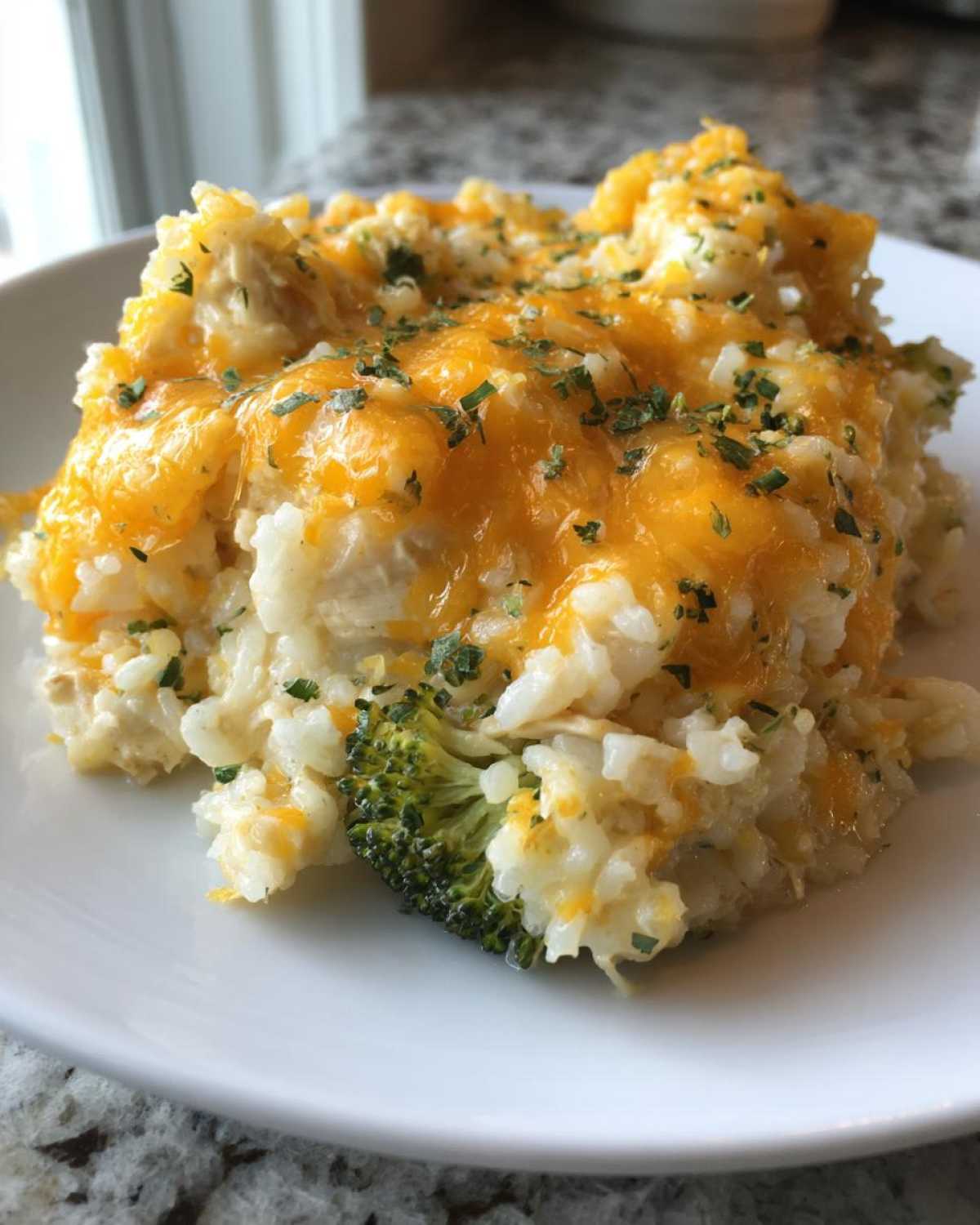 A serving of cheesy chicken and rice casserole topped with melted cheddar cheese and parsley, including a piece of broccoli.