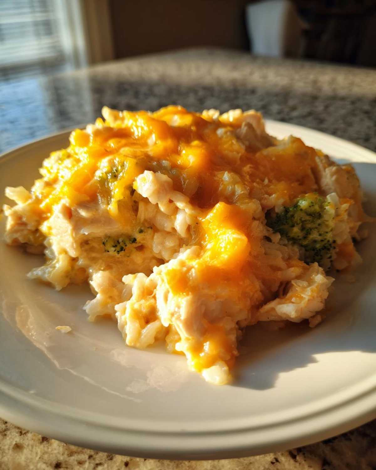 A close-up serving of cheesy chicken and rice mixed with broccoli florets, topped with melted cheddar cheese.