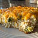 A close-up of a serving of cheesy chicken and rice with visible broccoli florets, topped with melted cheddar.