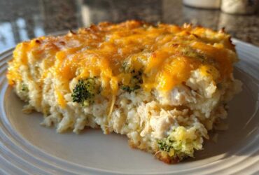 A close-up of a serving of cheesy chicken and rice with visible broccoli florets, topped with melted cheddar.
