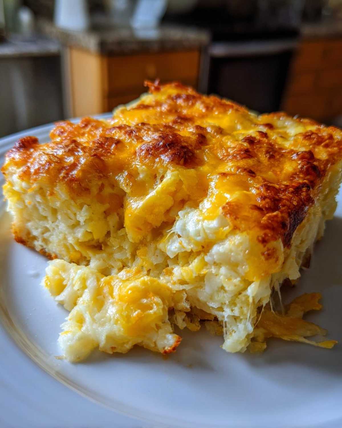 A close-up of a serving of cheesy potato casserole showing melted, browned cheese topping and stringy cheese pulls.