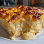 A close-up of a generous slice of cheesy potato casserole showing creamy interior and a deeply browned, cheesy crust.