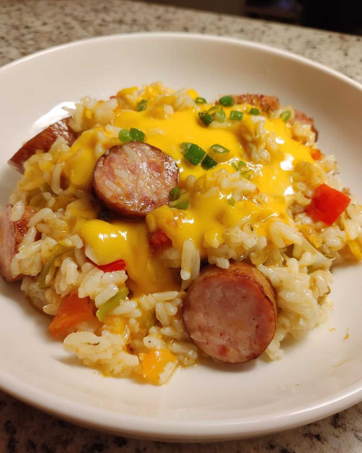 Close-up of cheesy sausage and rice mixed with vegetables, topped with melted cheese and green onions.
