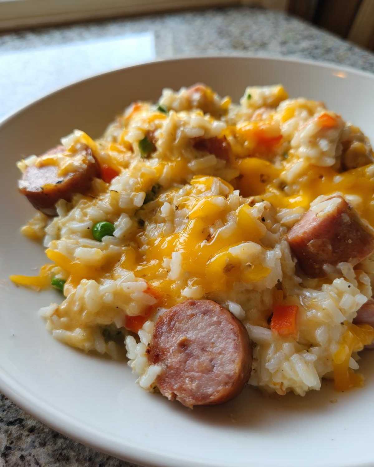 Close-up of cheesy sausage and rice mixed with vegetables served in a white bowl.