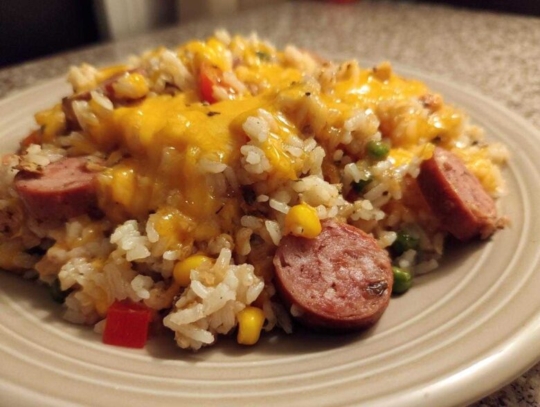 Close-up of cheesy sausage and rice mixed with corn and peas served on a beige plate.